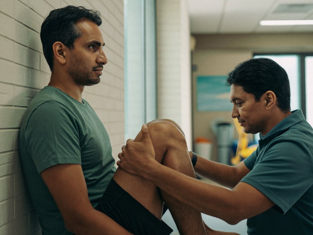 Physiotherapist examining an older man's knee during an assessment in a clinic