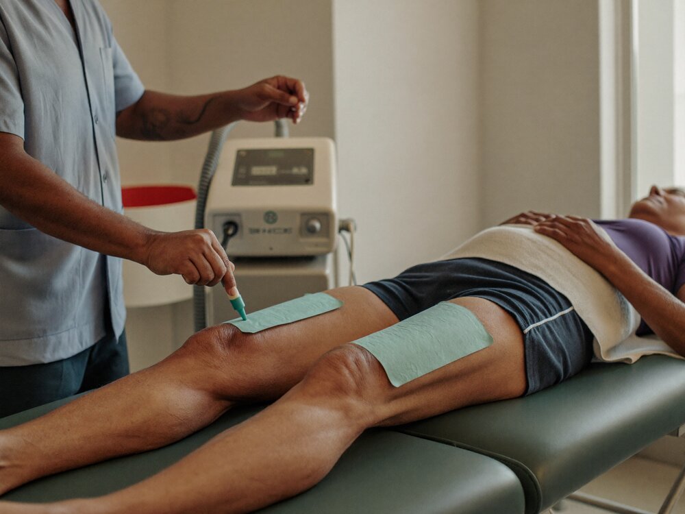 Physiotherapist positioning electrode pads over a patient's thigh with the stimulation unit alongside
